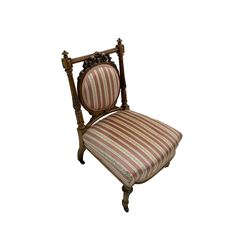 Late Victorian walnut framed nursing chair, fluted and foliate carved upright supports, circular cameo back with carved ribbon tie decoration, upholstered in striped fabric, on turned supports with brass and ceramic castors