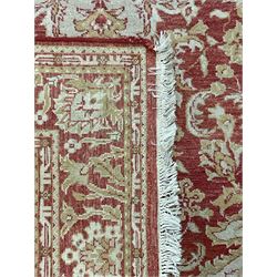 Persian design beige and crimson ground rug, the field decorated with interlacing scrolled foliage, repeating border within guard stripes 