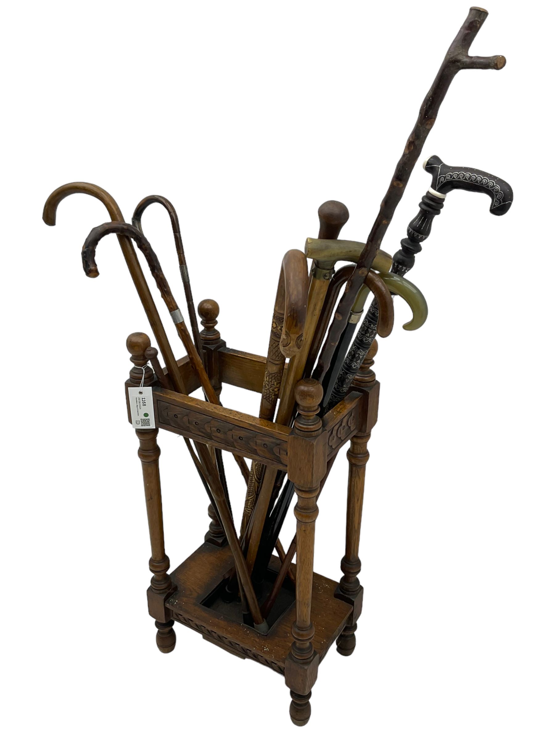 Early 20th century oak stick stand, rectangular structure with decorative carving, square base fitted with tray, on turned supports topped with finials; twelve assorted walking canes 