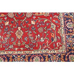 Persian Kashan crimson ground rug decorated with scrolling foliage, the indigo guard stripes with repeating stylised palmette motifs