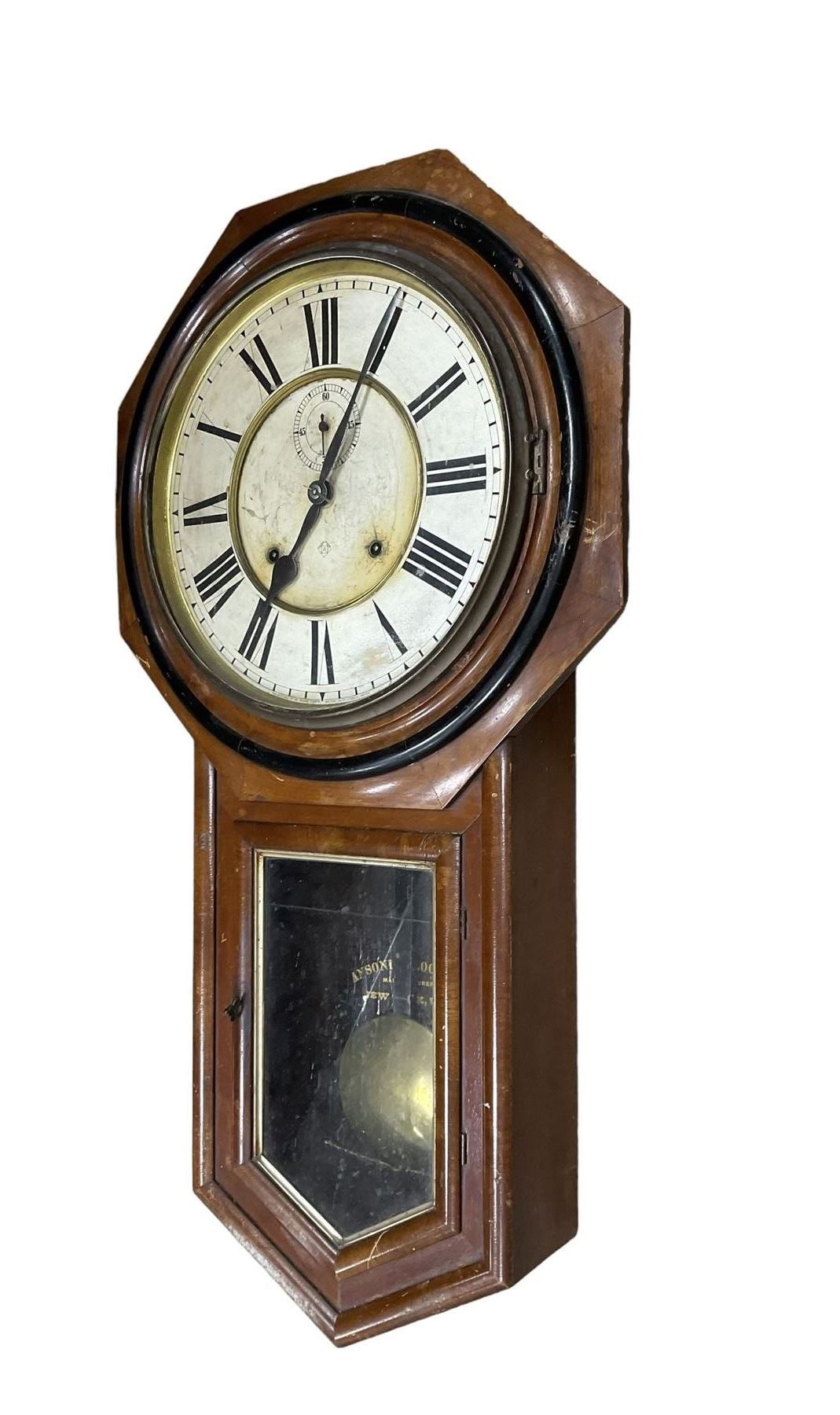 American - Late 19th century Ansonia 8-day wall clock, with a hexagonal wooden dial surround and circular spun bezel, glazed case door and visible pendulum,  two part dial with Roman numerals, minute track, spade hands and seconds dial, twin train spring driven movement striking the hours on a gong.