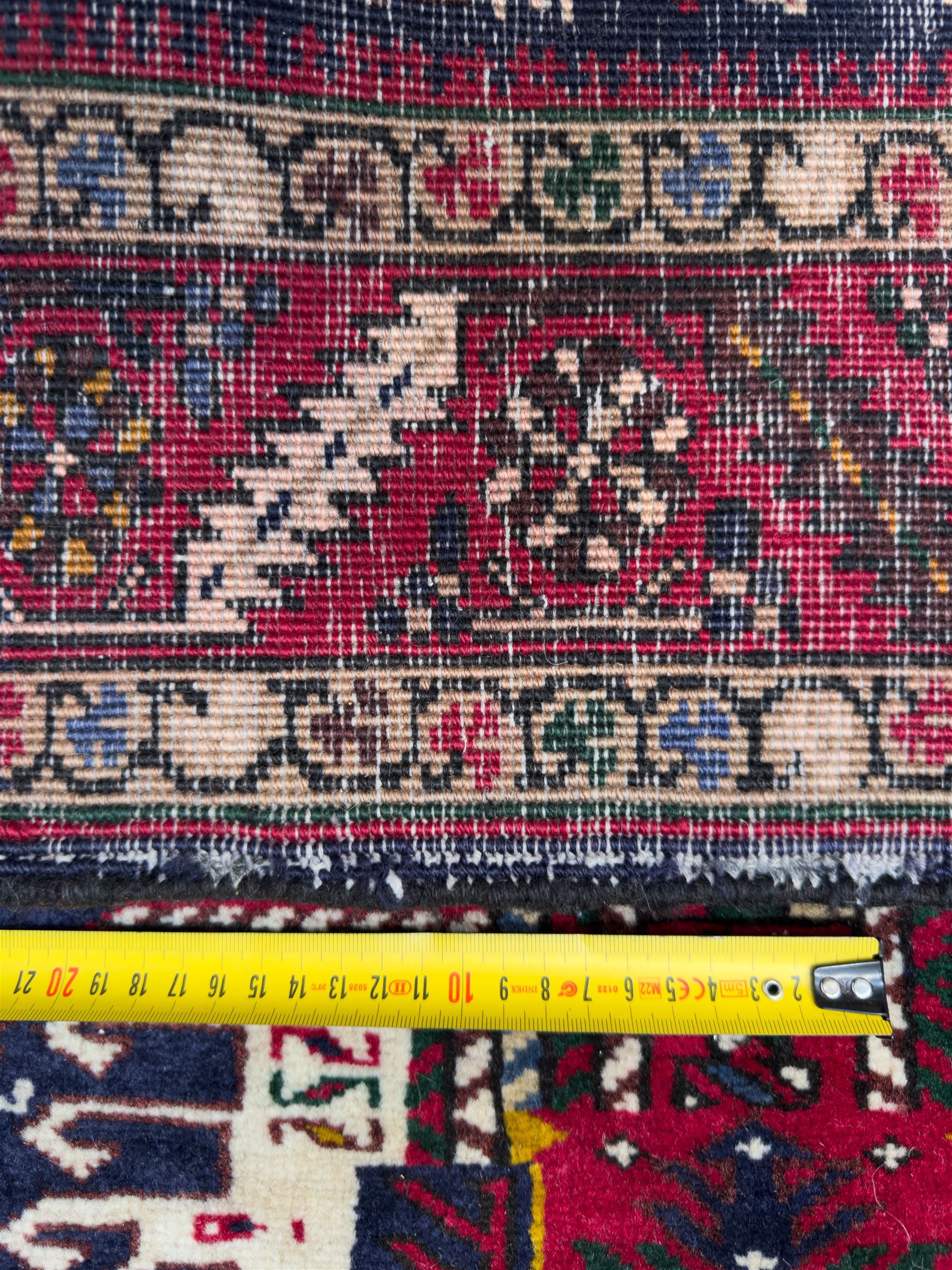 Northwestern Persian Heriz hand-knotted runner, dark indigo field with a series of linked stepped medallions in madder red, ivory, and green, flanked by angular floral motifs, within a madder red border of stylized rosettes and geometric vine motifs 405cm x 95cm