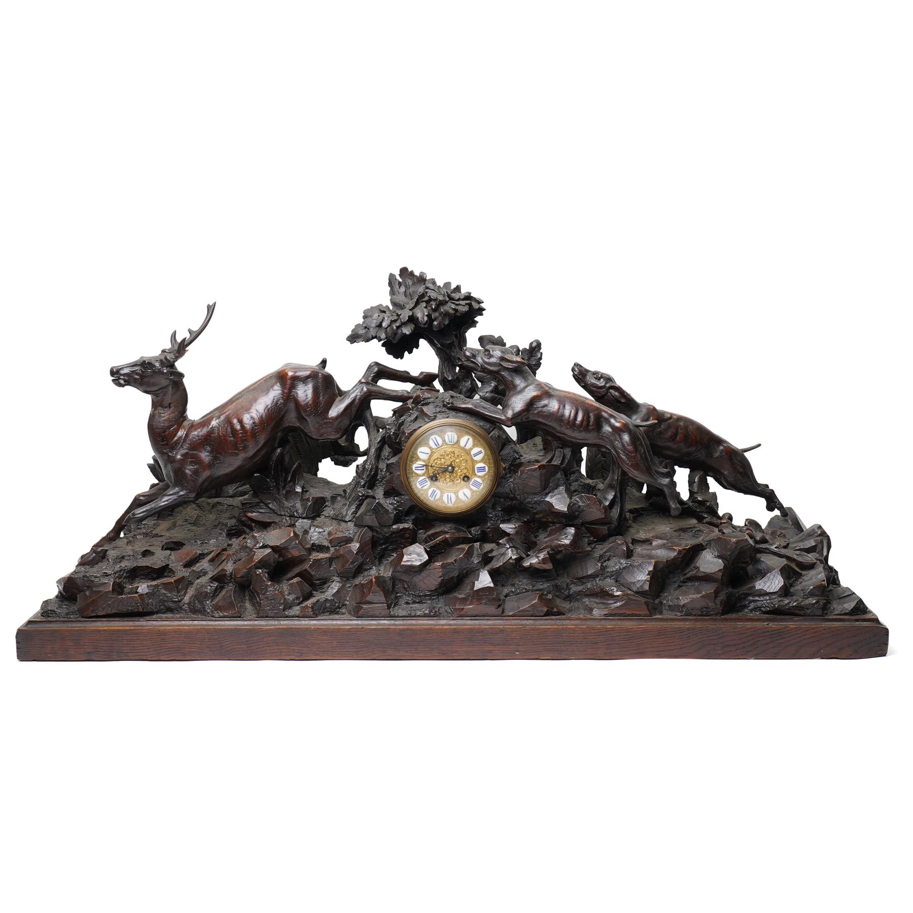 19th-century-8-day German Black Forest mantel clock c1880, with a carved oak case depicting a hunting scene with a stag pursued by hounds amidst rockwork and oak foliage, fitted with a French Parisian movement with a cast brass dial enclosed within a glazed brass bezel with a pendulum adjustment arbor, cartouche blue-on-white enamel  Roman numerals, engraved five minute Arabic's and contrasting steel Fleur-di-Lis hands, twin train going barrel movement with a recoil anchor escapement and countwheel strike. With pendulum.  