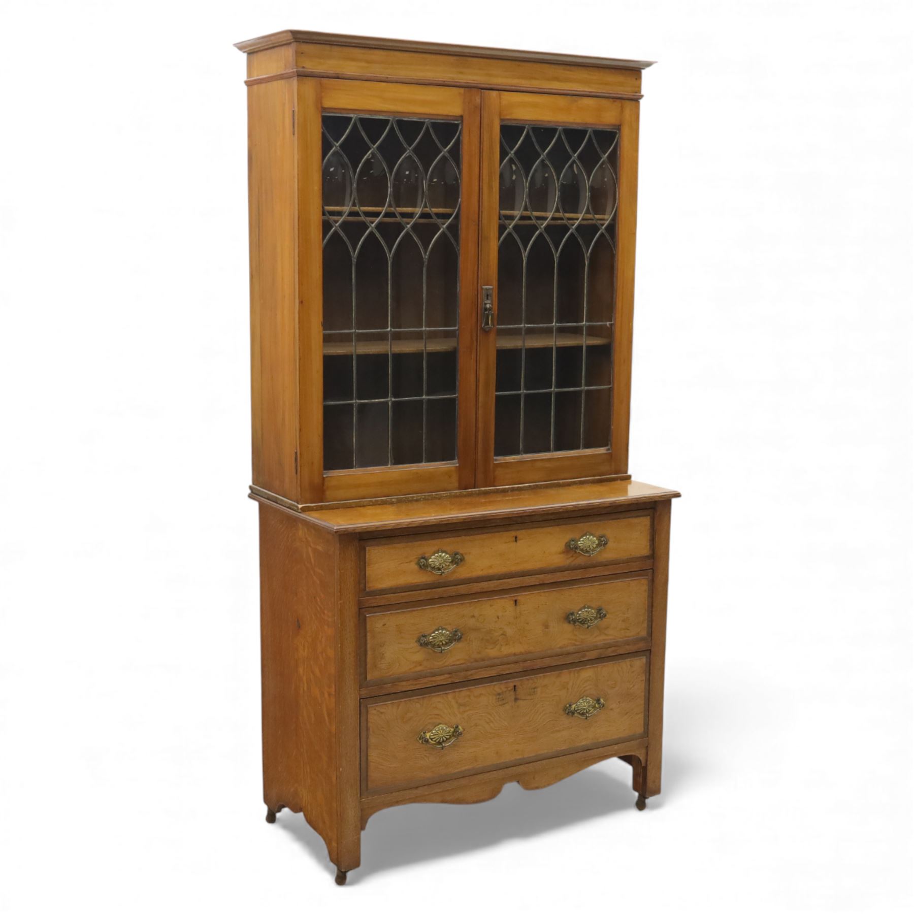 20th century wooden bookcase cabinet, fitted with a pair of leaded glass panel doors opening to adjustable shelves, the base top and front veneered in richly figured walnut, contrasted with solid oak panelled sides and shaped lower frieze, terminating in castors