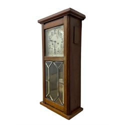 German - Art Deco oak cased 8-day wall clock c 1930, with a moulded flat top and fully glazed door, deeply cut bevelled glass panels and visible pendulum, silvered dial with Art Deco design spandrels, Arabic numerals, minute track and spade hands, twin train movement striking the hours and half hours on four gong rods. With pendulum and key.  
