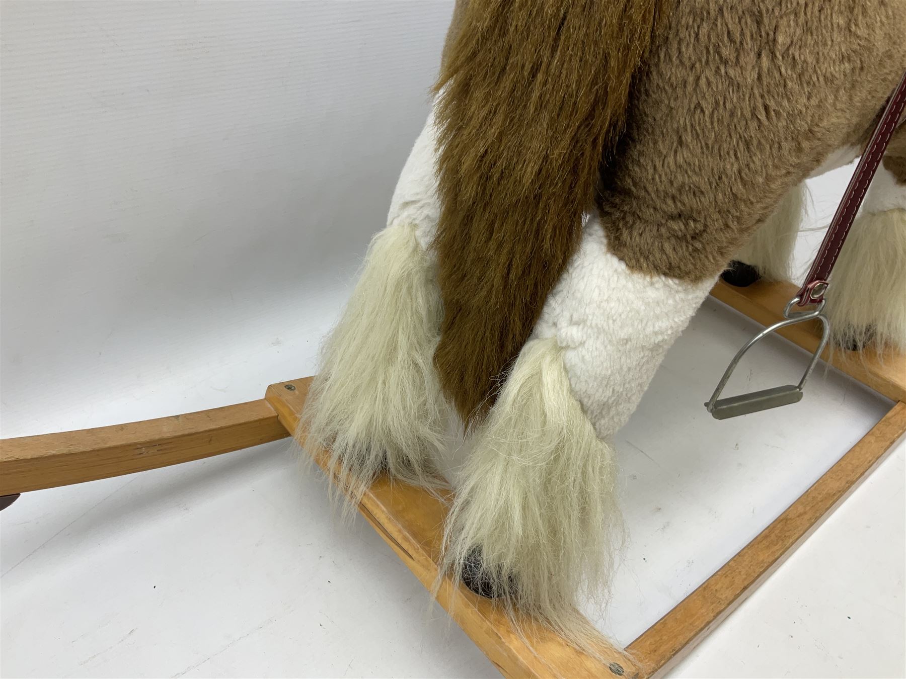 Modern plush covered rocking horse with inset eyes, simulated leather bridle and saddle with metal stirrups, on curving wooden rockers L94cm H64cm