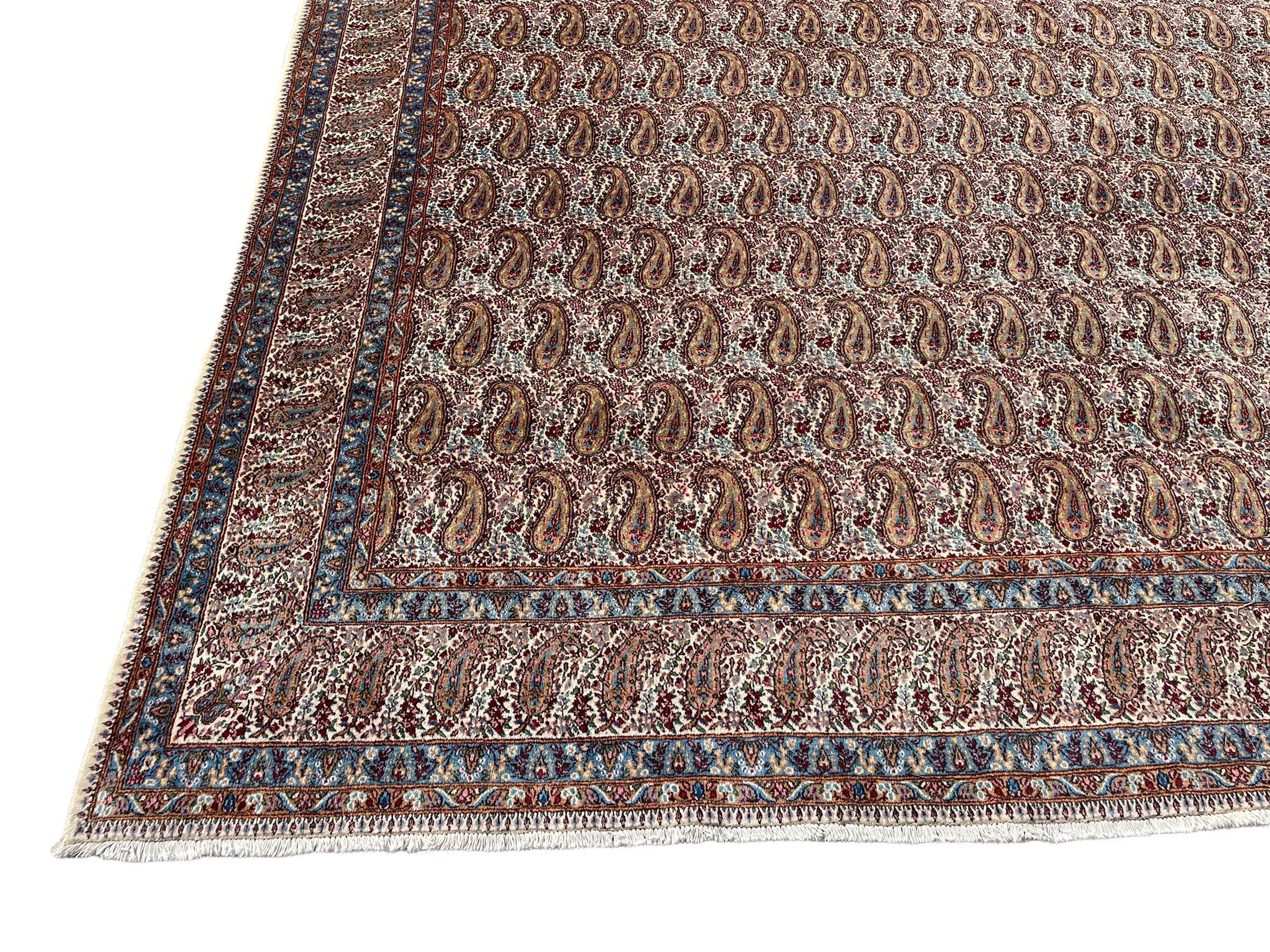 Persian Kirman carpet, the ivory ground field and border decorated with repeating Boteh motifs, interspaced with all-over floral design, blue ground border guards, the top border with signature panel