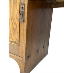 Arts and Crafts period twin pedestal desk, arching pediment on spindle supports, raised shelf on moulded rectangular top with leather inset, fitted with central drawer and two cupboards, the doors with lead glazed panes, pressed copper handle plates 