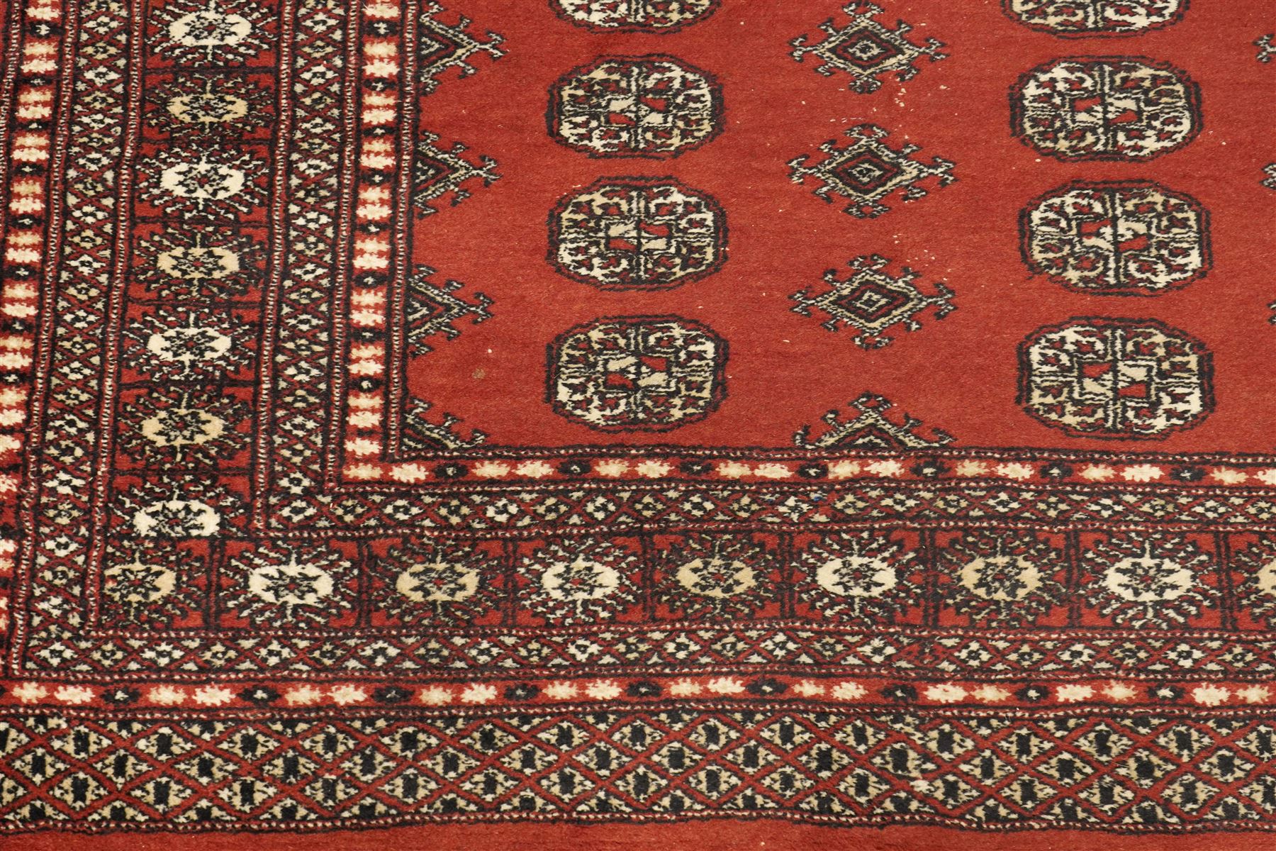 Turkoman hand-knotted rug, madder red ground with two rows of repeating octagonal guls interspersed with geometric motifs, enclosed by multiple geometric and stylised floral borders, with fringed ends