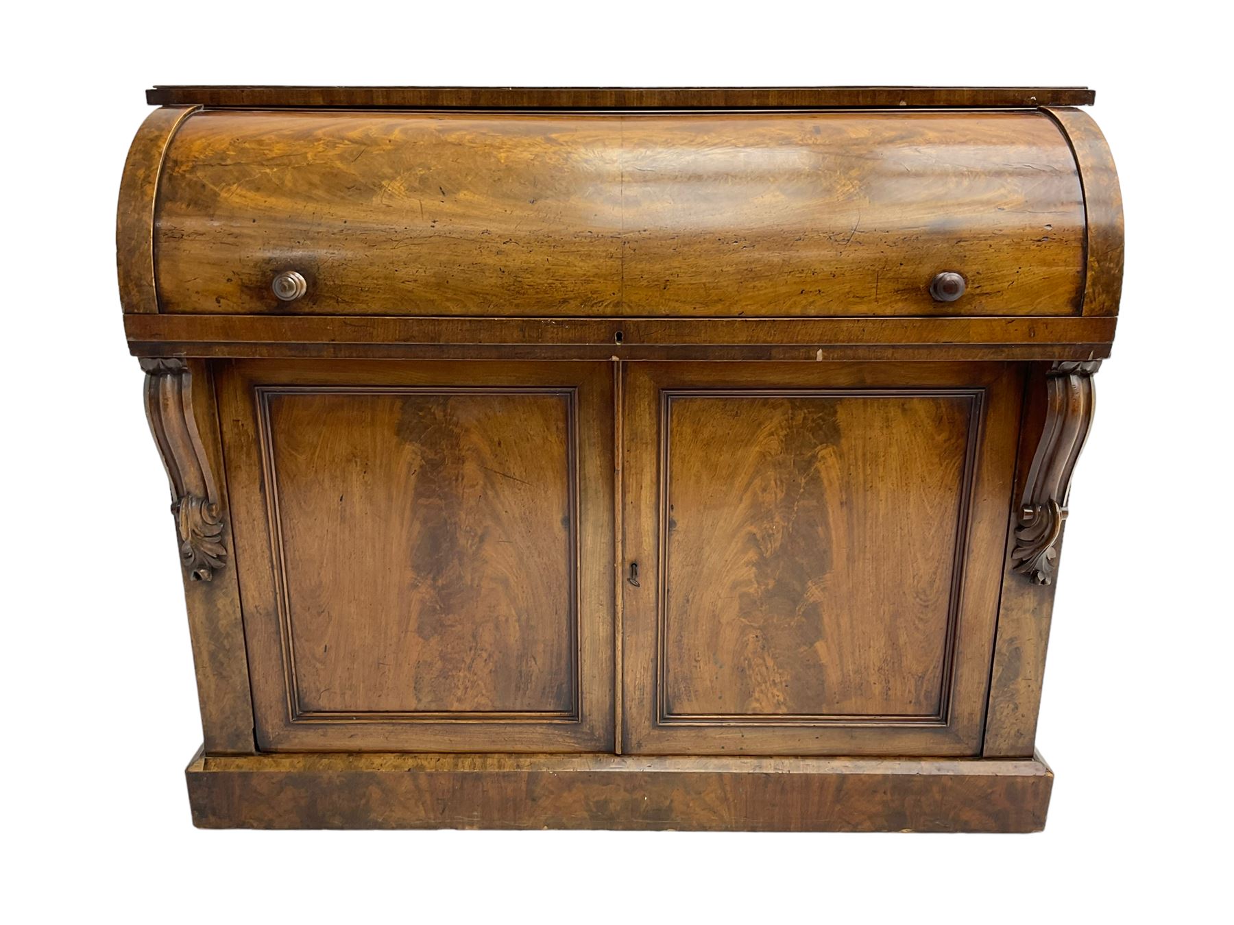 Victorian mahogany roll-top writing desk, top concealing fitted interior with pigeonholes and three drawers, the trisector inset writing surface with writing slope, base fitted with panelled cupboard enclosing single shelf, decorated with scrolled corbels