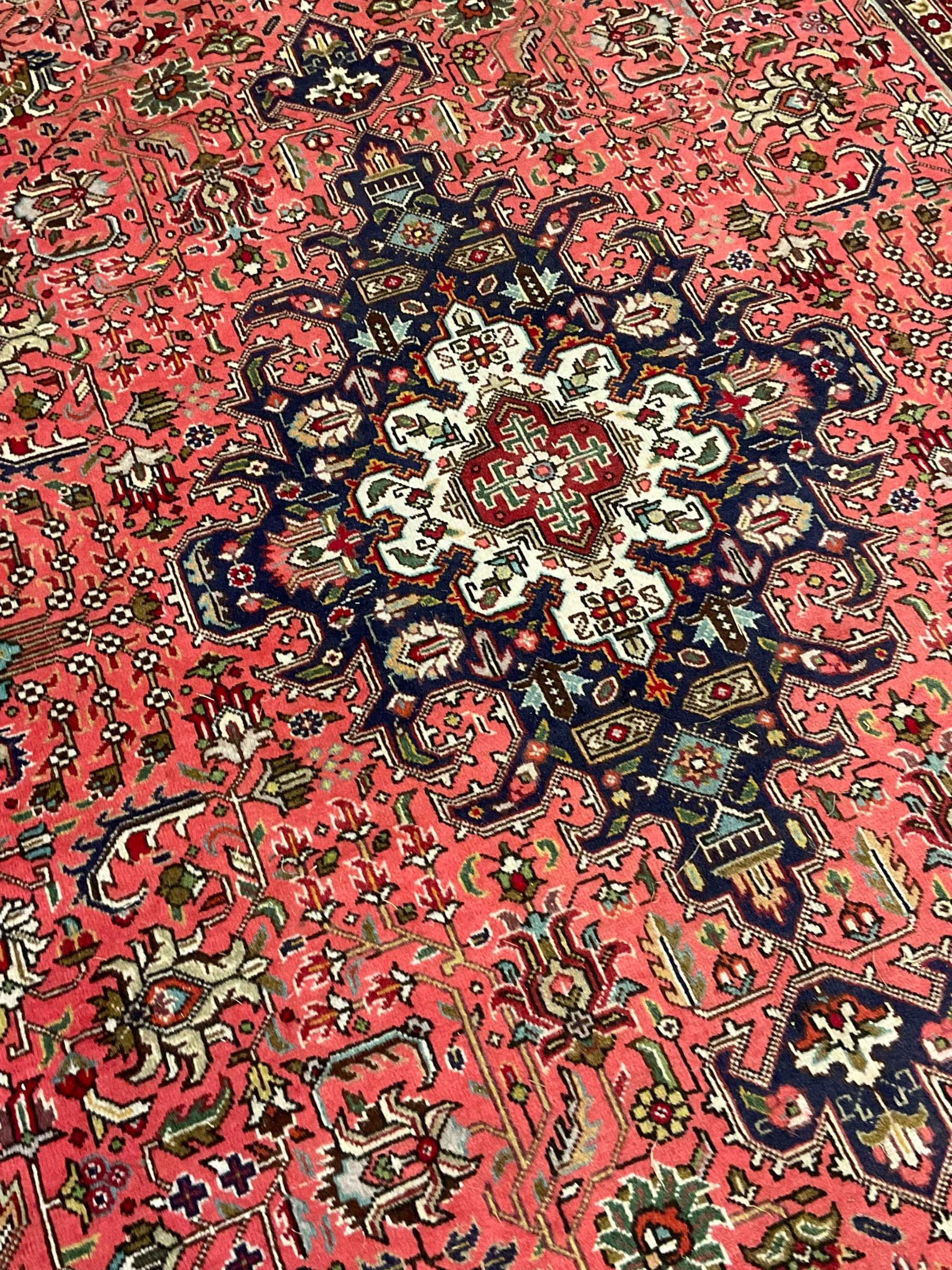 North West Persian pink ground Tabriz carpet, central indigo ground medallion surrounded by stylised plant motifs and trailing foliage, the main border with overall floral design within guard stripes 