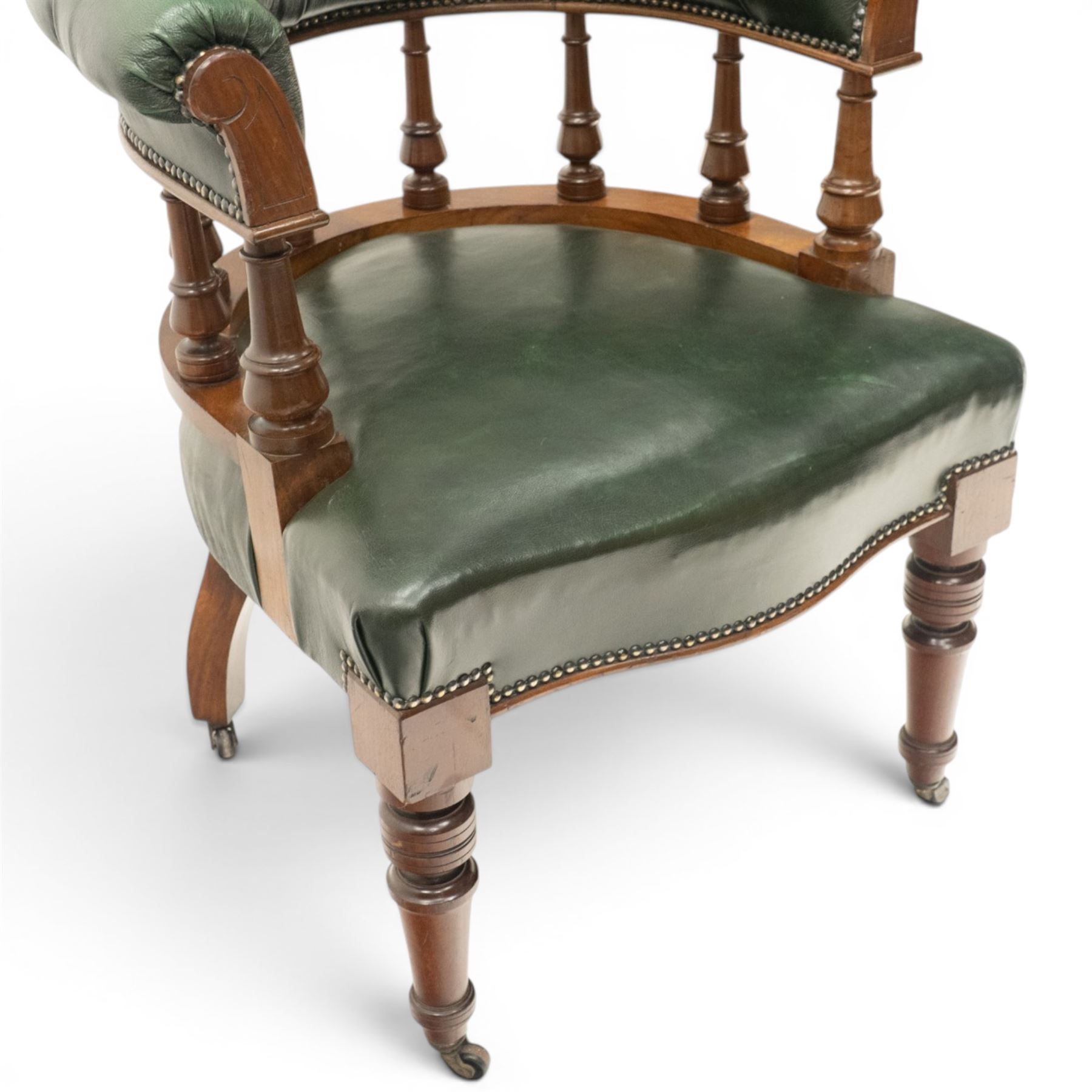 Late Victorian mahogany framed Captains tub desk chair, the green leather upholstered cresting rail over turned spindle supports over a sprung seat, raised on front turned supports terminating to ceramic castors