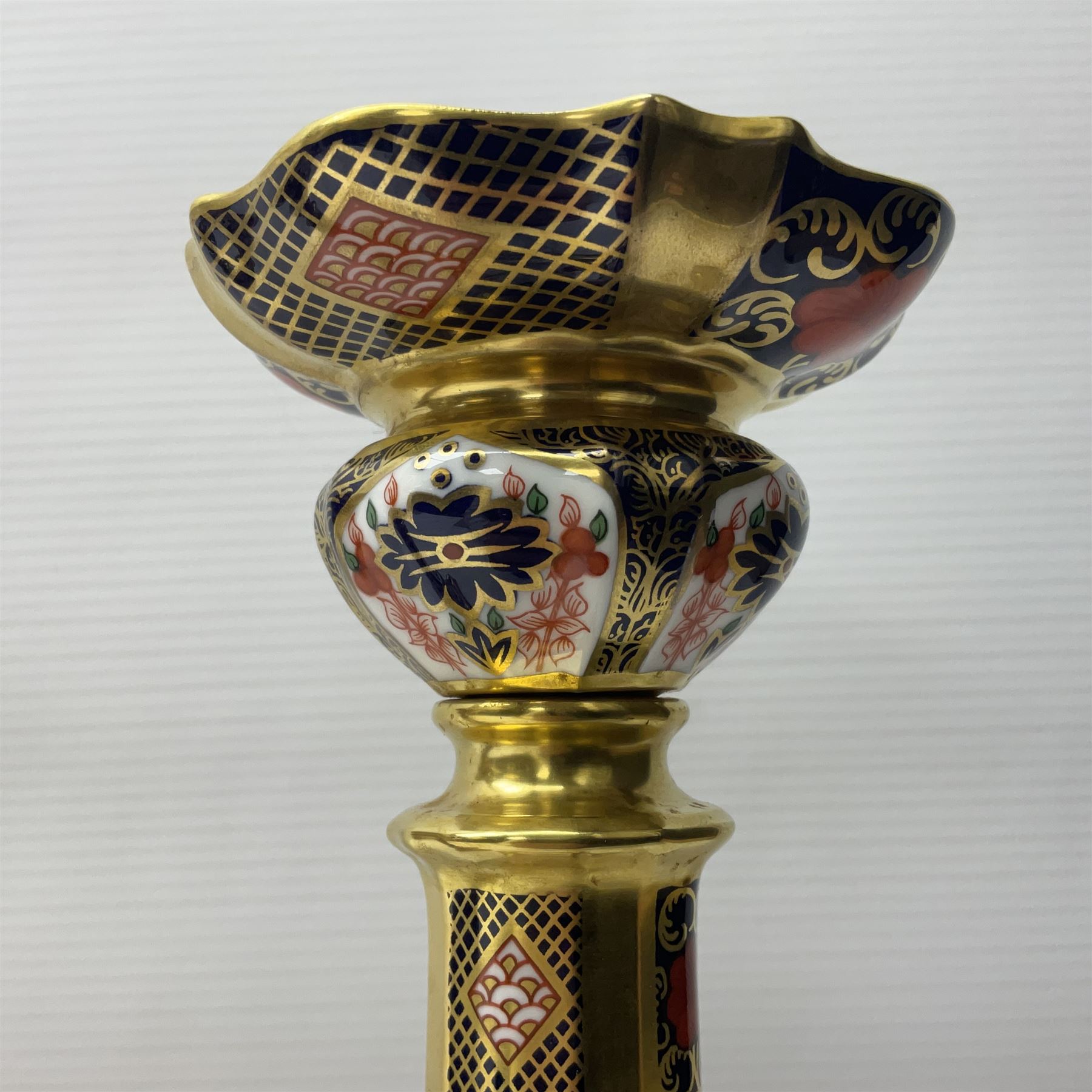 Pair of modern Royal Crown Derby Old Imari 1128 pattern candlesticks, each with shaped drip tray affixed to squat socket, upon spreading stem and canted square base with gilt dolphin edges, with printed marks beneath including Roman numeral year cypher for 2003, H26.5cm, with original boxes