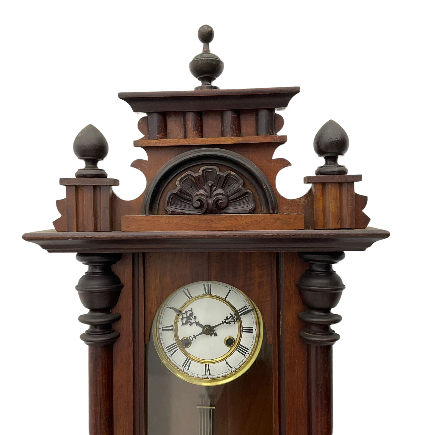 A late 19th century German wall clock with an 8-day spring driven movement striking the hours on a coiled gong, in a mahogany case with a shaped pediment and turned columns flanking a full-length glazed door, with a two-part dial enamel with Roman numerals, minute track and pierced gothic designed hands, gridiron pendulum and beat plate. With Key.




