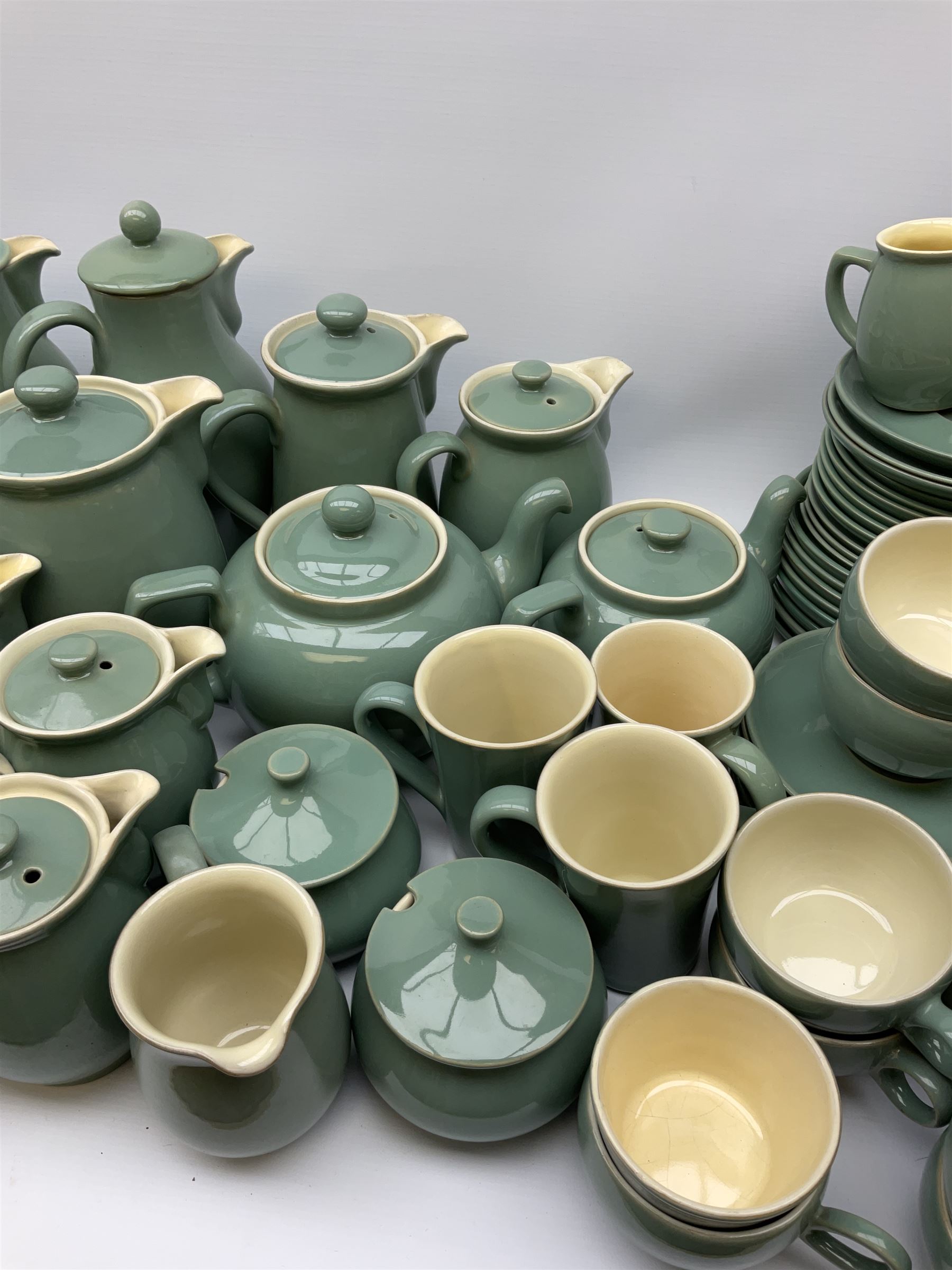 Denby Manor Green pattern tea service, comprising of three teapots, twelve coffee pots of various sizes, four hot water jugs with lids, seven jugs, eleven teacups, four mugs, seventeen saucers, six sugar bowls, two sugar bowls with lids and eleven side plates.  