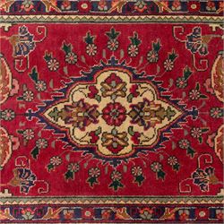 North West Persian Tabriz hand-knotted runner, madder red field with central octagonal medallions of sage green, navy and ivory, ground enclosing a floral rosette and radiating angular vinery, scrolling floral sprays and palmettes either end with shaped pendants principal border on navy ground decorated with a continuous vine-scroll of palmettes and rosettes, flanked by narrow guard borders, with cotton fringe ends 