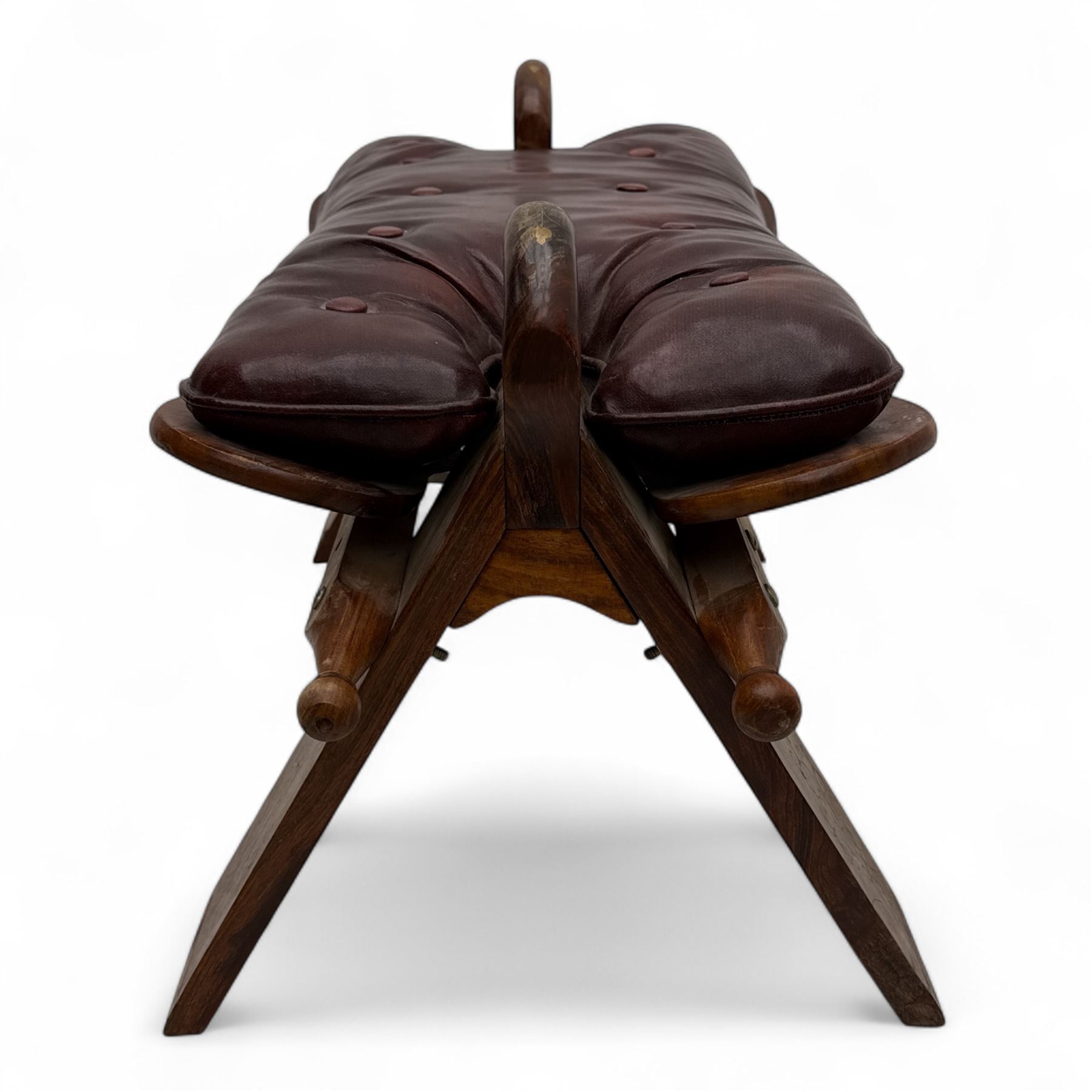 Pair of early 20th century Anglo-Indian camel saddle stools, with deep buttoned red leather upholstered seats and horn-shaped pommels, on X-form supports with turned ball finials