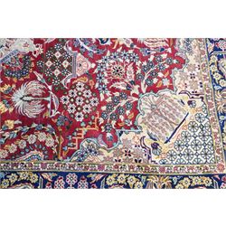 Central Persian Najafabad hand-knotted carpet, crimson field with a central elaborate cusped medallion with radiating floral motifs, surrounded by finely drawn scrolling vines incorporating stylized palmettes and rosettes, flowering plants and vase motifs, ivory spandrels similarly decorated enclosed by a dark indigo main border of floral arabesques between multiple guard stripes, with cotton fringe ends 
