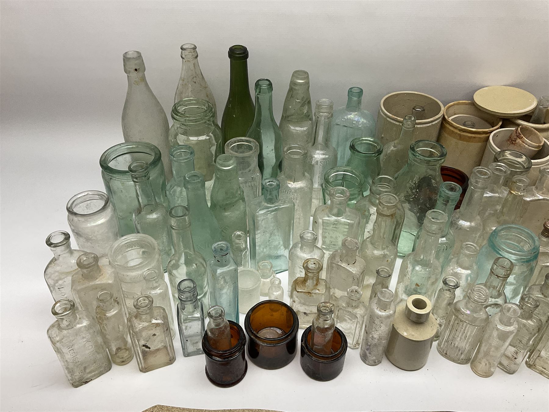 A collection of assorted glass bottles, of various size and form, mostly clear and green glass examples, plus a small group of Stoneware jars. 