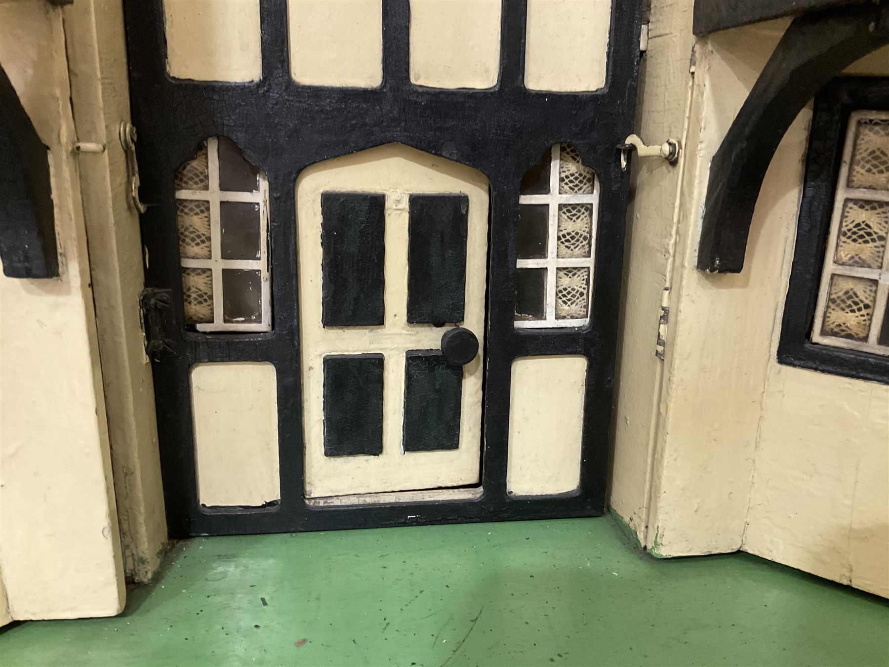 Large Tri-ang No.93 doll`s house in the 'Stockbroker's Range' c1935; two-storey double-fronted Tudor design, half timbered gables, two-storey bay windows, cream and mock shrubbery to front, opening metal framed windows with green shutters, red simulated tiled roof with chimney, integral garage with opening doors, front elevation has four hinged doors opening to reveal two bedrooms with fire places, living room, bathroom and kitchen with built in dresser and sink, entrance hall and staircase, side entrance with porch and seat and sun dial over on chimney stack; some wiring for electrical lighting; metal Tri-ang Toys disc verso; comprehensively furnished H66cm L117cm D43cm