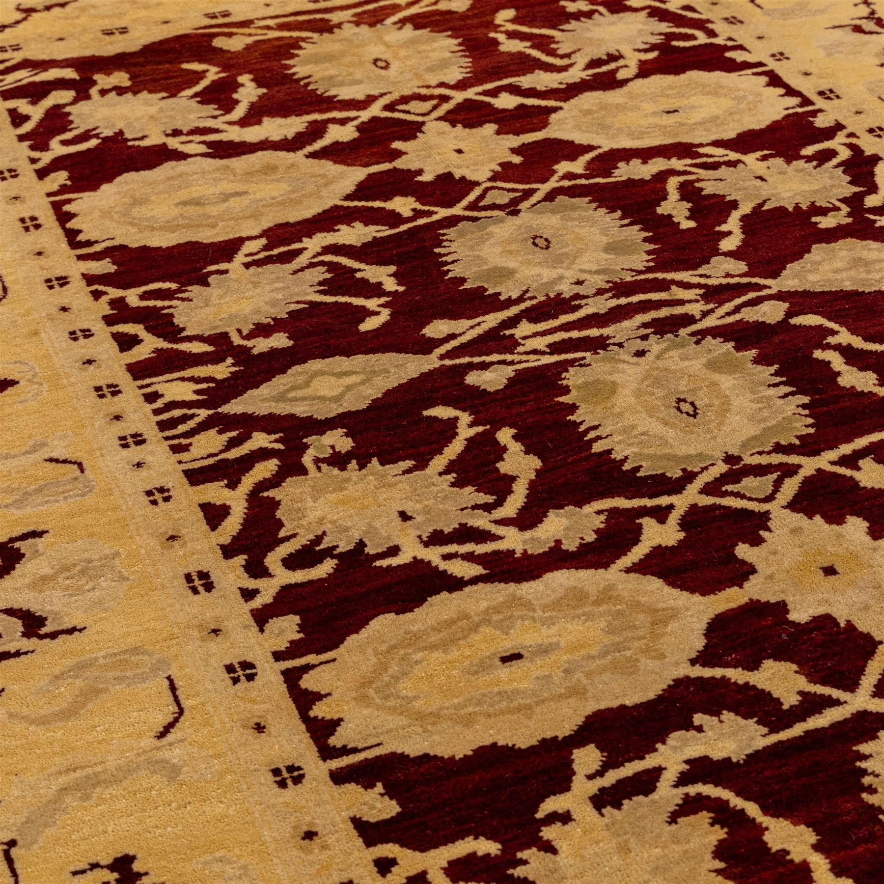 Ziegler design hand knotted wool rug, the rich red ground woven with oversized floral medallions and angular vine scrolls, framed by a contrasting ivory border of repeating floral ornament and minor guard stripes, with fringed ends