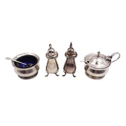1920s silver two piece cruet set, comprising mustard pot and cover and open salt, of circular form with shaped rim, hallmarked William Suckling Ltd, Birmingham 1924, with blue glass liners and two matched hallmarked silver condiment spoons, together with a pair of silver pepper shakers, of typical baluster form, engraved with initial, upon four pad feet, hallmarked Walker & Hall, Birmingham 1918
