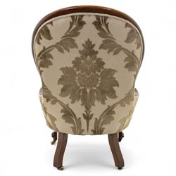 Victorian mahogany framed spoon back armchair, the shaped and padded back over serpentine seat upholstered in a floral damask pattern fabric within a moulded frame carved with scrolled arms, raised upon cabriole front legs with scroll feet on porcelain castors 