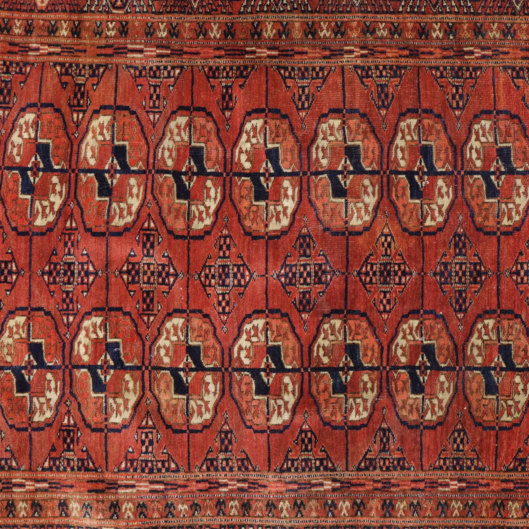 Central Asian Turkmen Tekke hand-knotted rug, madder red field decorated with rows of octagonal guls linked by secondary motifs within a dense geometric border, with fringe ends  