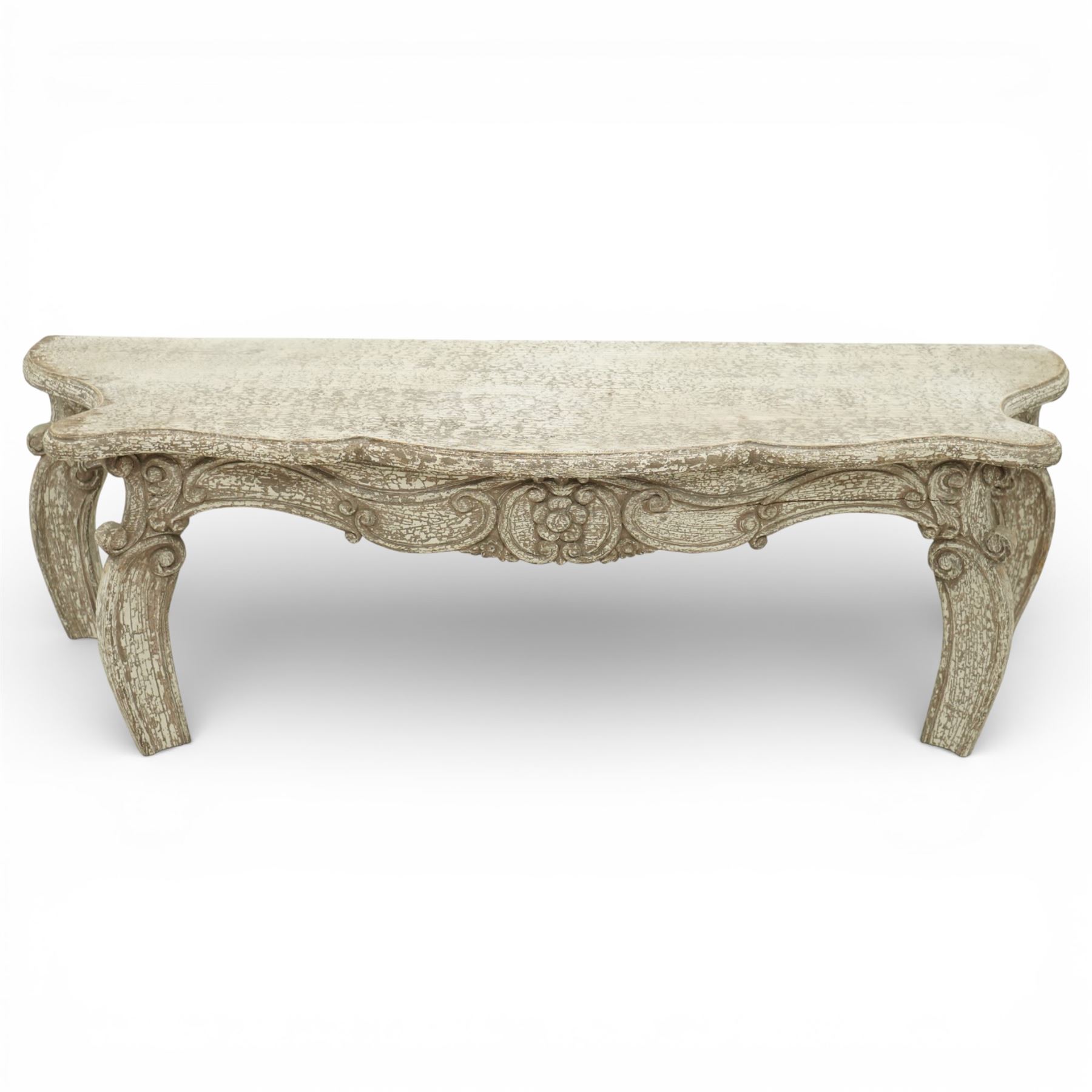 French style low console table, the shaped rectangular top with undulating outline and moulded edge, worn painted finish throughout, the frieze carved with flowing C-scrolls, shell and foliate detail centred by a floral reserve, on cabriole legs with carved knees and inward curving feet
