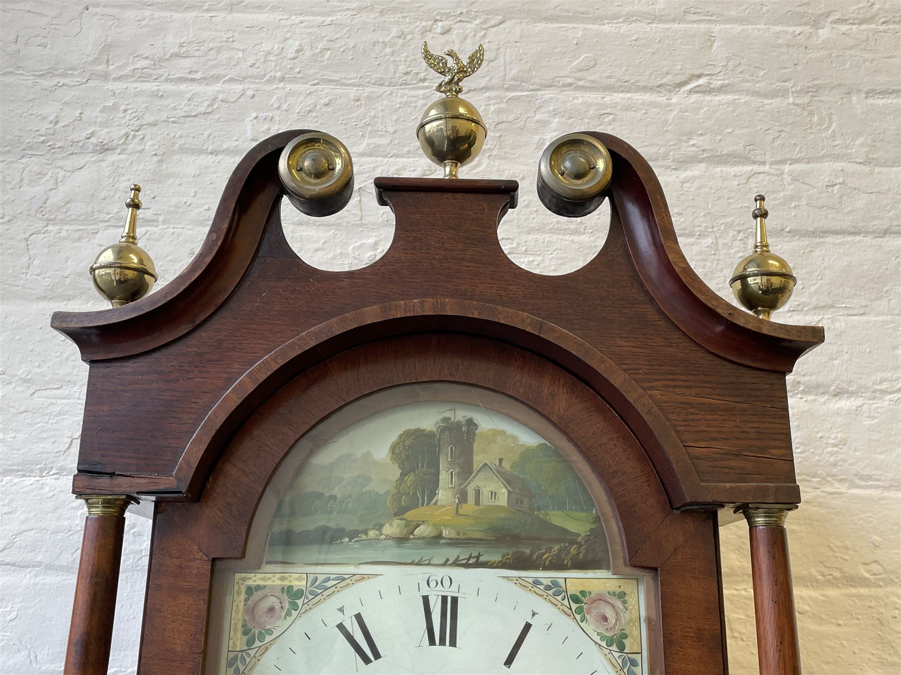 Thirty-hour oak cased longcase clock by  William Bancroft of Scarborough circa 1830, with a swan’s neck pediment, brass patera and three brass spire and ball finials, stepped break arch hood door flanked by plain pillars with brass capitals, trunk with a full length door and curved arch top, on a plain square plinth with bracket feet, painted break arch dial with roman numerals and quarter hour Arabic’s, date recorder (anti clockwise) and matching brass hands, arch painted with a rural scene depicting a ruined tower and cottage with depictions of flowers to the spandrels, dial pinned directly to a chain driven countwheel striking movement, striking the hours on a bell. With weight and pendulum. The Bancroft family were prodigious Scarborough clockmakers during the 18th and 19th century, William Bancroft is recorded as working in Newborough Street from 1820 onwards. 


