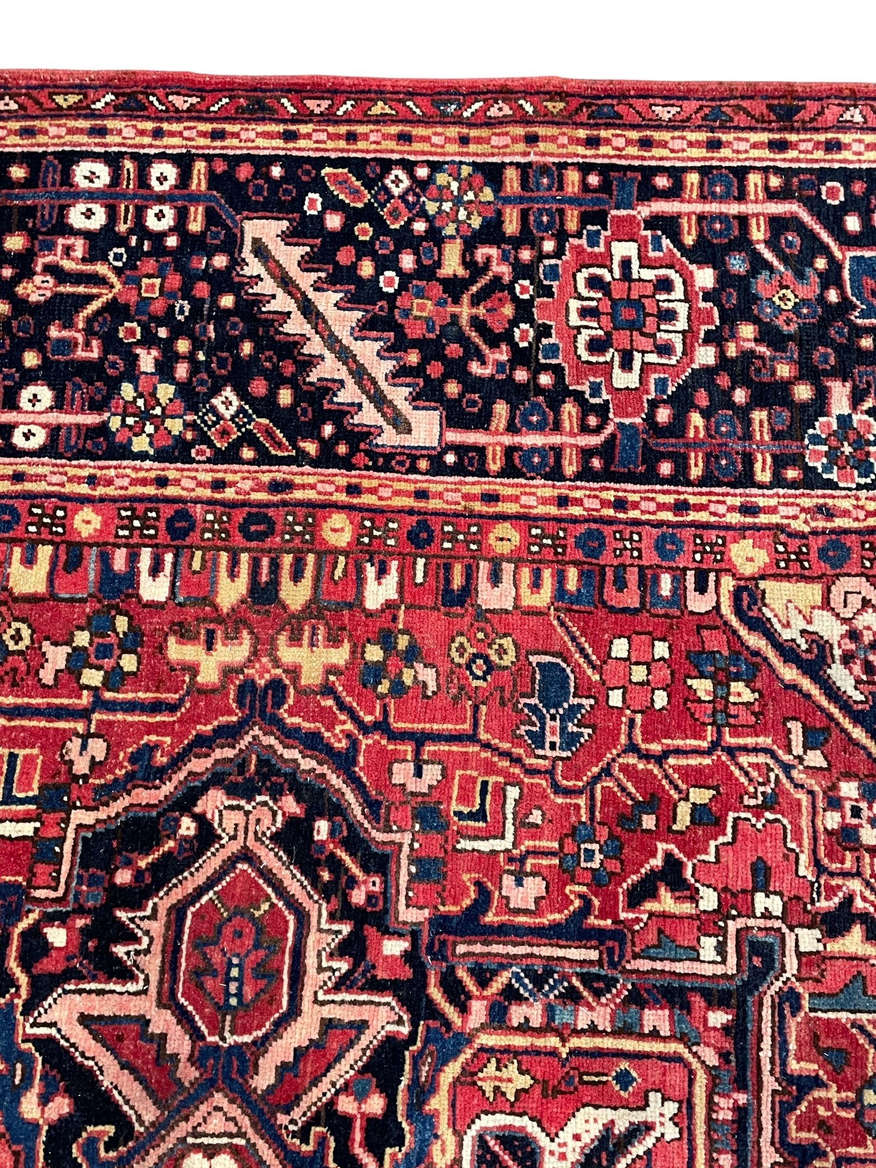 Persian Heriz crimson ground carpet, large central medallion comprising projecting palmettes with surrounding stylised plant motifs and trailing branches, the main border decorated with stylised leaf and flower head motifs within geometric pattern guard stripes