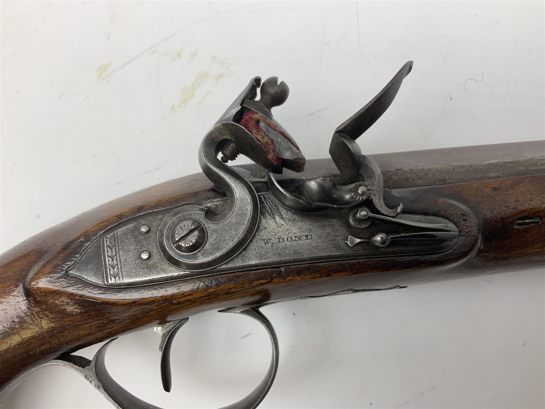 Early 19th century flintlock 16-bore overcoat/duelling pistol by William Bond Lombard Street London, the 23cm octagonal brown stub twist damascus barrel with small foresight, two barrel pins and ram rod under, inscribed Lombard Street London to the top and W. Bond to the action, full walnut stock with lightly engraved steel furniture, pineapple finial and escutcheon, half cock facility L39cm; loose mounted on later mahogany display stand with trade label