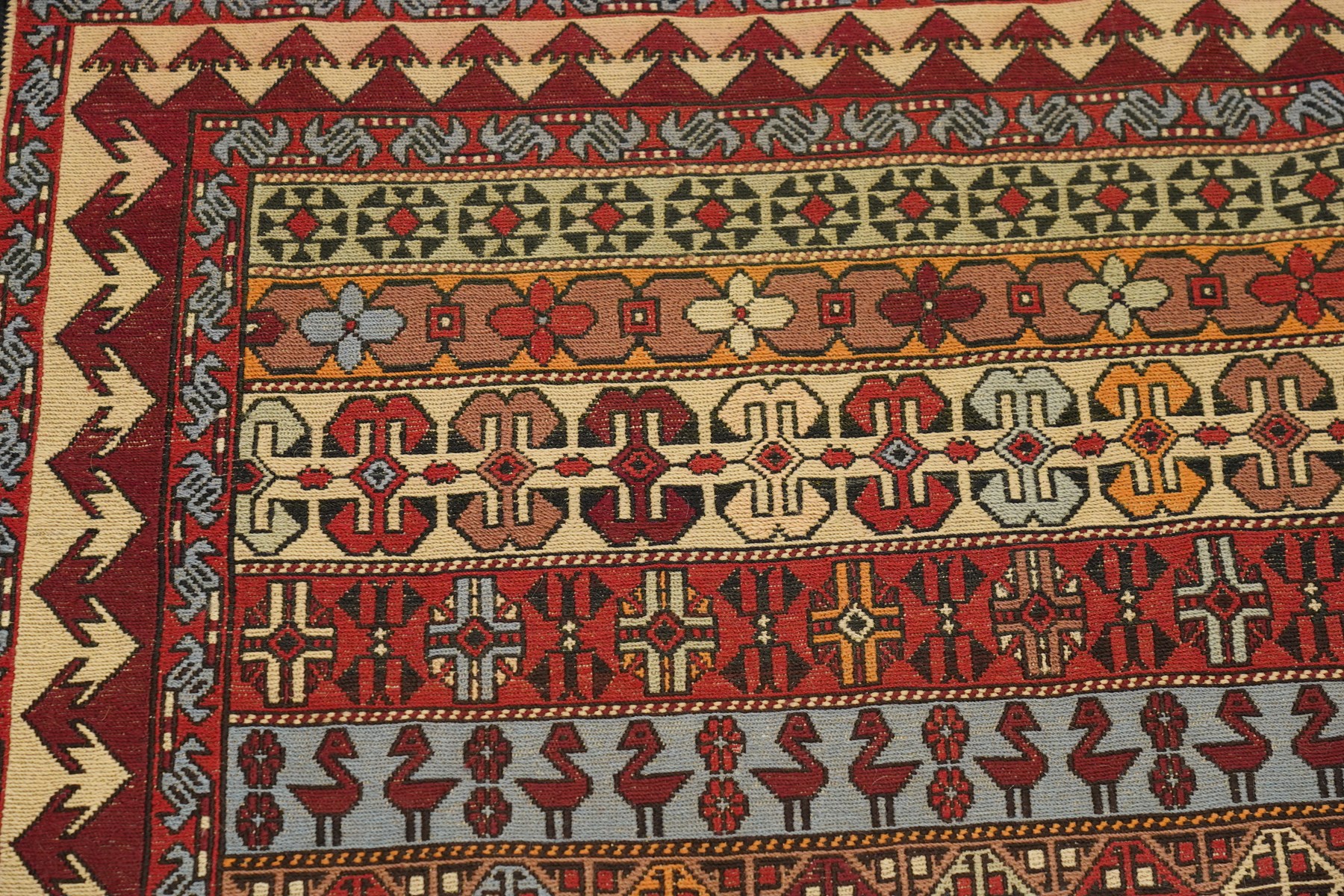 
Oman tribal design rug, field decorated with horizontal bands of stylised birds, flowerheads, stars and hooked geometric motifs in red, ivory, ochre and pale blue, enclosed by serrated ivory and red borders and narrow patterned guard stripes