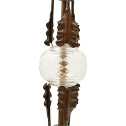 Arts and Crafts wrought iron and copper standard lamp, the openwork stem centred by a cut-glass reservoir with arrow-cut decoration, applied with stylised copper leaves, on shaped tripod base