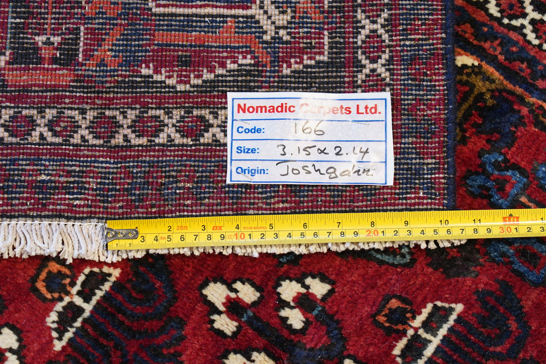 Central Persian Joshaghan hand-knotted carpet, deep red field decorated with a lattice design of stylized boteh and palmette motifs arranged around a stepped diamond medallion, navy corner spandrels similarly decorated enclosed by a dark indigo main border of floral and geometric motifs between multiple guard stripes, with cotton fringe ends 