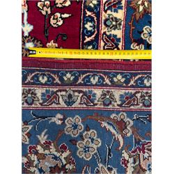 Central Persian Yazd hand-knotted rug, madder red field with scrolling vines, palmettes, and rosettes around a cusped lozenge medallion within a blue ground border of palmettes and flowerheads, 366cm x 250cm