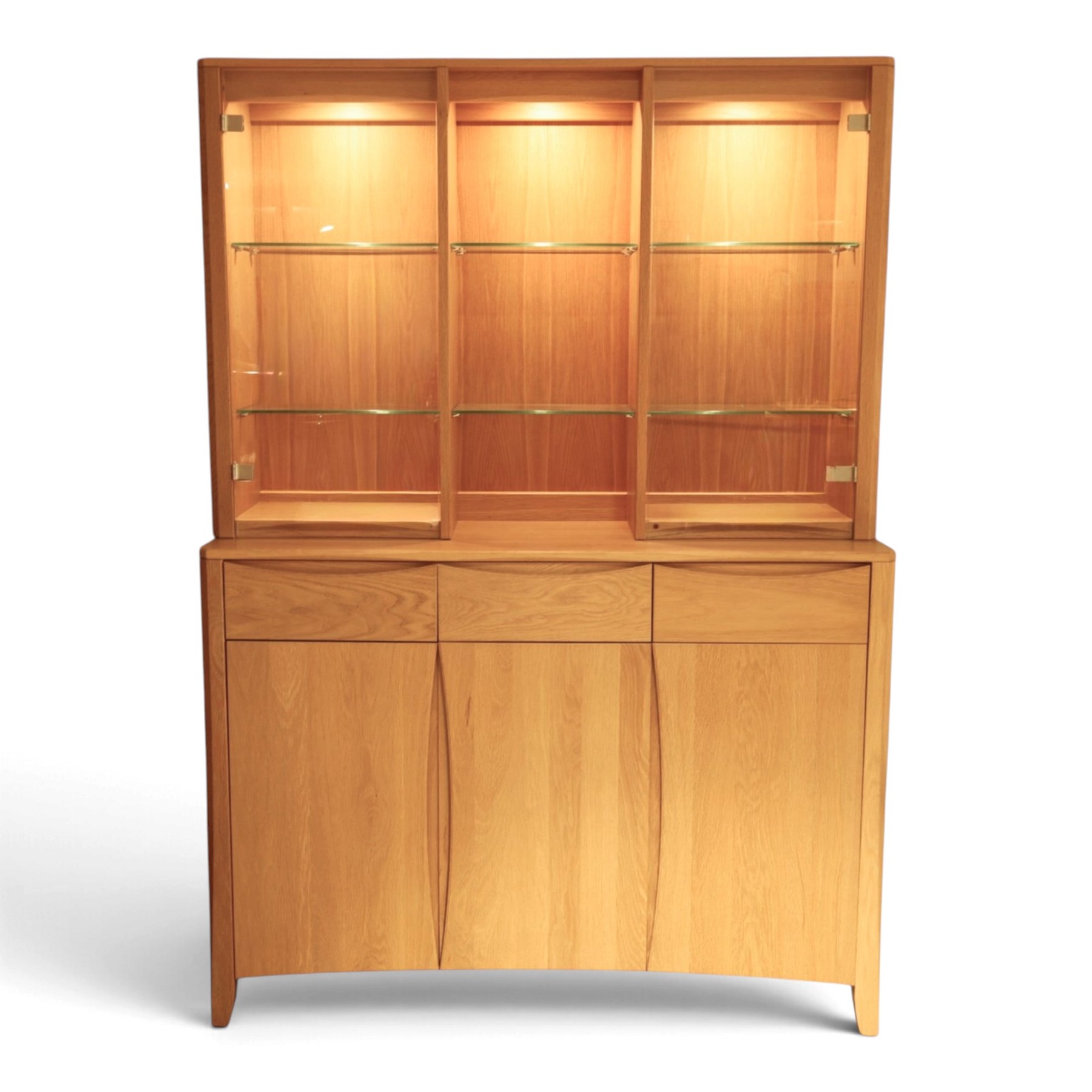 Ercol - 'Artisan' light oak dresser, upper section with cantered corners, with central open area fitted with adjustable glass shelves, flanked by twin glazed cabinets with further adjustable glass shelving, the lower section with three shorts drawers with recessed handles, above three cupboard doors with recessed handles enclosing adjustable wooden shelves, raised on short tapering supports 