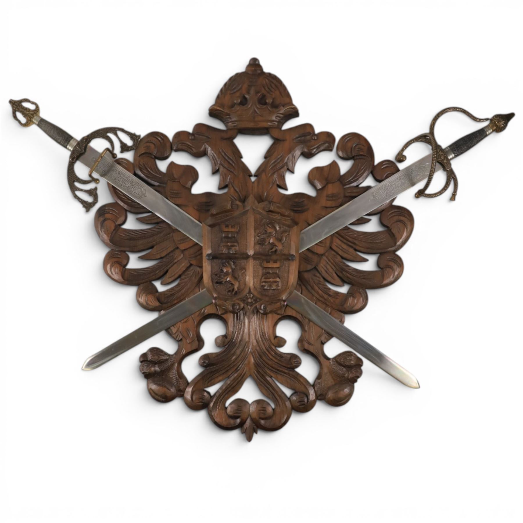 Carved wooden wall plaque, decorated with foliate scrolls, with two reproduction swords attached, together with five other wooden plaques with foliate scrolls and shields