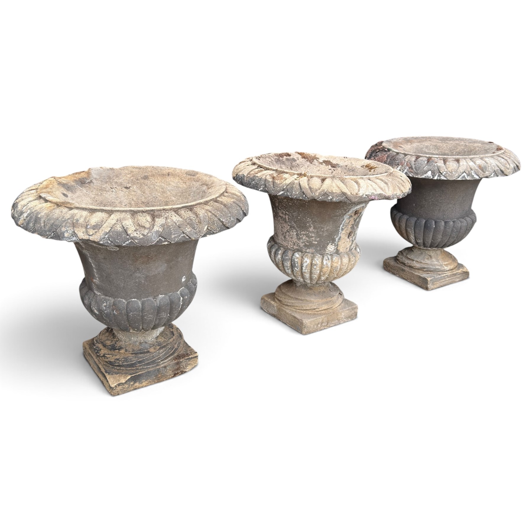 Set of three 19th century weathered carved sandstone garden urns of Neoclassical campana form, the broad everted rim carved with pointed egg-and-dart motifs, above a plain waisted bowl with gadrooned underbelly, on moulded rope-twist socle and square plinth base