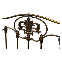 Victorian design king size brass bed frame, featuring an arched headboard and footboard with intricate cast floral and scrollwork centre motifs, flanked by cylindrical supports with ball finials and decorative collars, raised on rounded feet, with a slatted wooden base