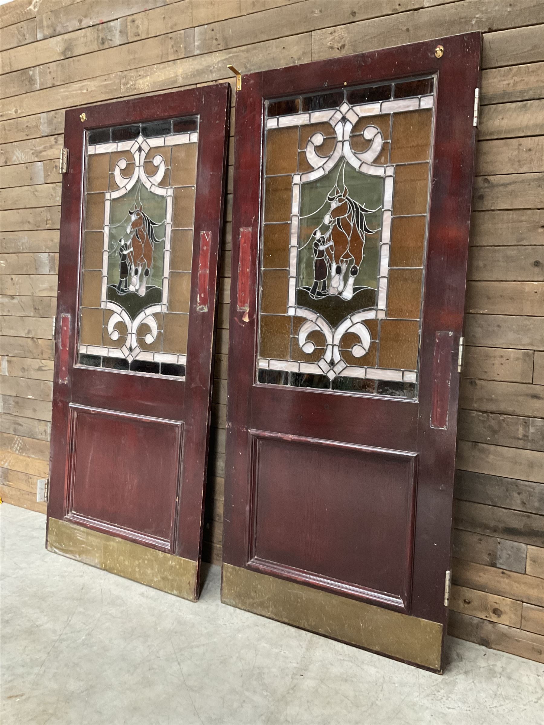 Two early to mid 20th century timber doors, set with lead framed stained glass panels depicting agricultural worker and horse