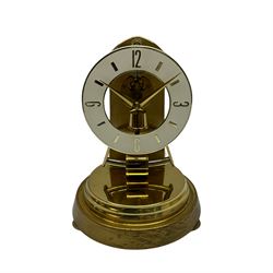 A  late 20th century German Kieninger & Obergfell, “Kundo” battery operated 
mantle clock under an acrylic shade, with an electrically operated solenoid pendulum housed on a 16cm circular brass base with three adjustable feet, skeleton movement with a visible escapement through an 4-1/2” open chapter ring dial, with gilt baton hands, three-hour numerals and baton markers.  H30cm 




