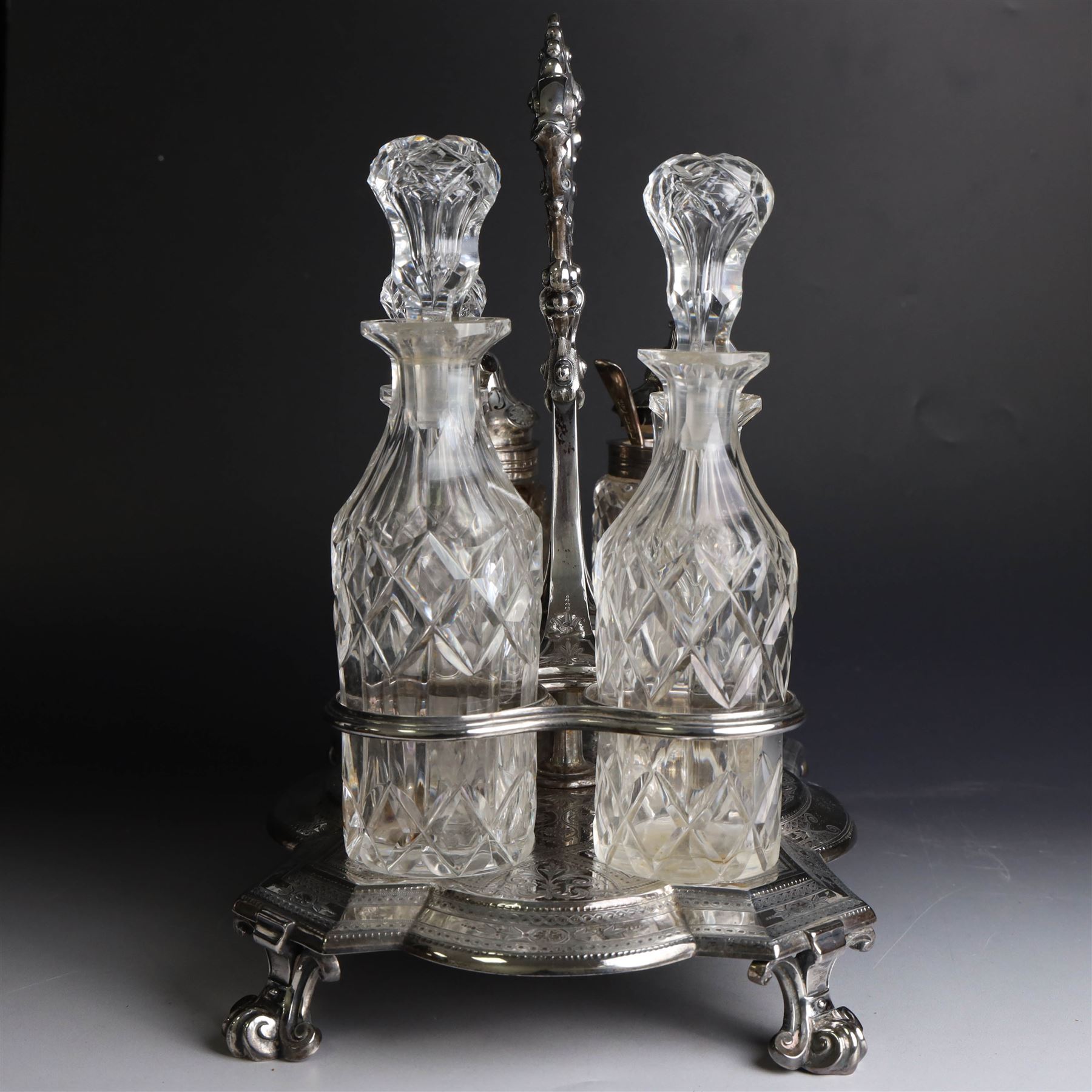 Victorian silver cruet stand, containing eight cut glass cruet bottles, four with silver covers, upon a shaped base with four scroll feet and loop handle, chased with floral and foliate decoration, the stand, base and bottle caps all hallmarked John, Edward, Walter & John Barnard, London 1872, one bottle with a matched silver cruet spoon, stand H30cm