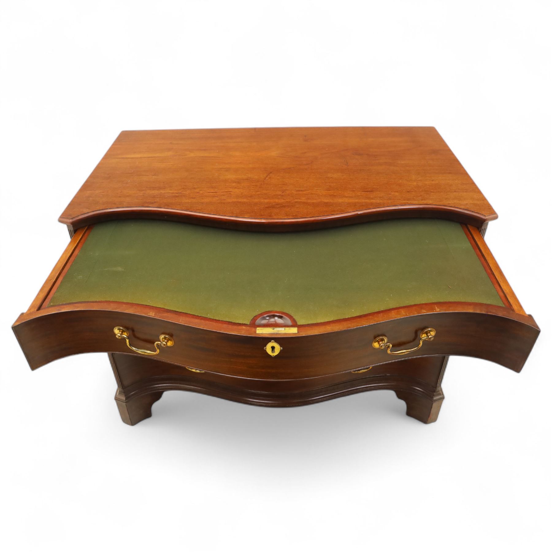 George III mahogany serpentine chest, moulded top over four cock-beaded drawers, the top drawer fitted with baize lined slide opening to reveal divisions,  enclosed by canted and fluted upright corners, the drawer fronts fitted with brass swan neck handles and circular plates with oval escutcheons, lower moulded edge over bracket feet, on lignum vitae castors