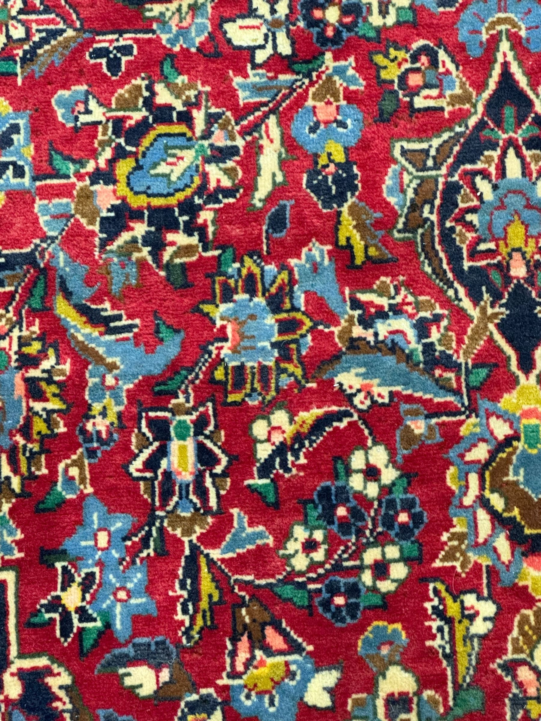 Central Persian Kashan crimson ground rug, central indigo pole medallion surrounded by sparsely placed bouquets interconnected with foliate branches, the guarded border with repeating palmette and Boteh motifs with interwoven scrolling patterns, framed by guard stripes