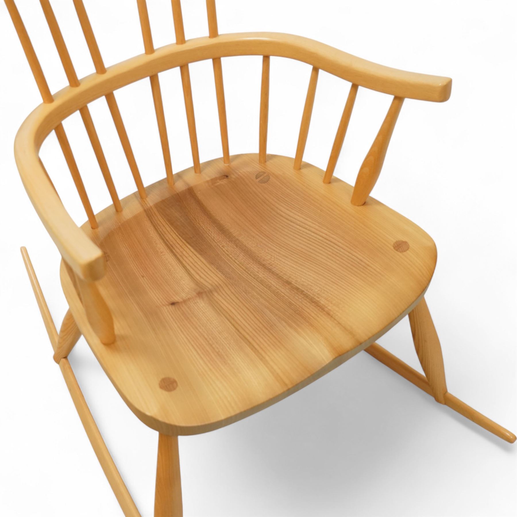Mid 20th century Windsor ash rocking armchair, in the manner of Ercol, with curved cresting rail above nine stick spindles, shaped and chamfered paddle arms, figured shaped seat, raised on turned legs joined by twin side stretchers and mounted on curved rockers