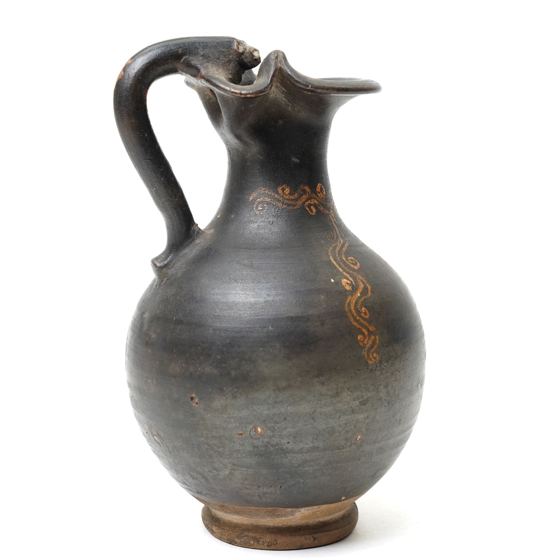 South Italian Gnathian terracotta oinochoe (jug) Apulian or Campanian (Late 4th century BC c.325-300 BC) of elegant ovoid form with trefoil mouth and single strap handle, the handle terminating in a stylised serpentine motif merging into the pouring lip, the vessel covered in a black gloss slip and decorated in added red, white and yellow with a theatrical mask, fillets and scrolling Dionysiac vine motifs, H19cm 
Notes: Gnathian ware takes its name from Egnathia in Apulia and is characterised by a black-gloss ground with added-colour decoration; the theatrical mask, fillets and vine scrolls relate to Dionysiac imagery associated with the symposium and theatre in South Italian Greek culture of the late fourth century BC. A very similar oinochoe is held in the The Metropolitan Museum of Art, object number 76.12.8