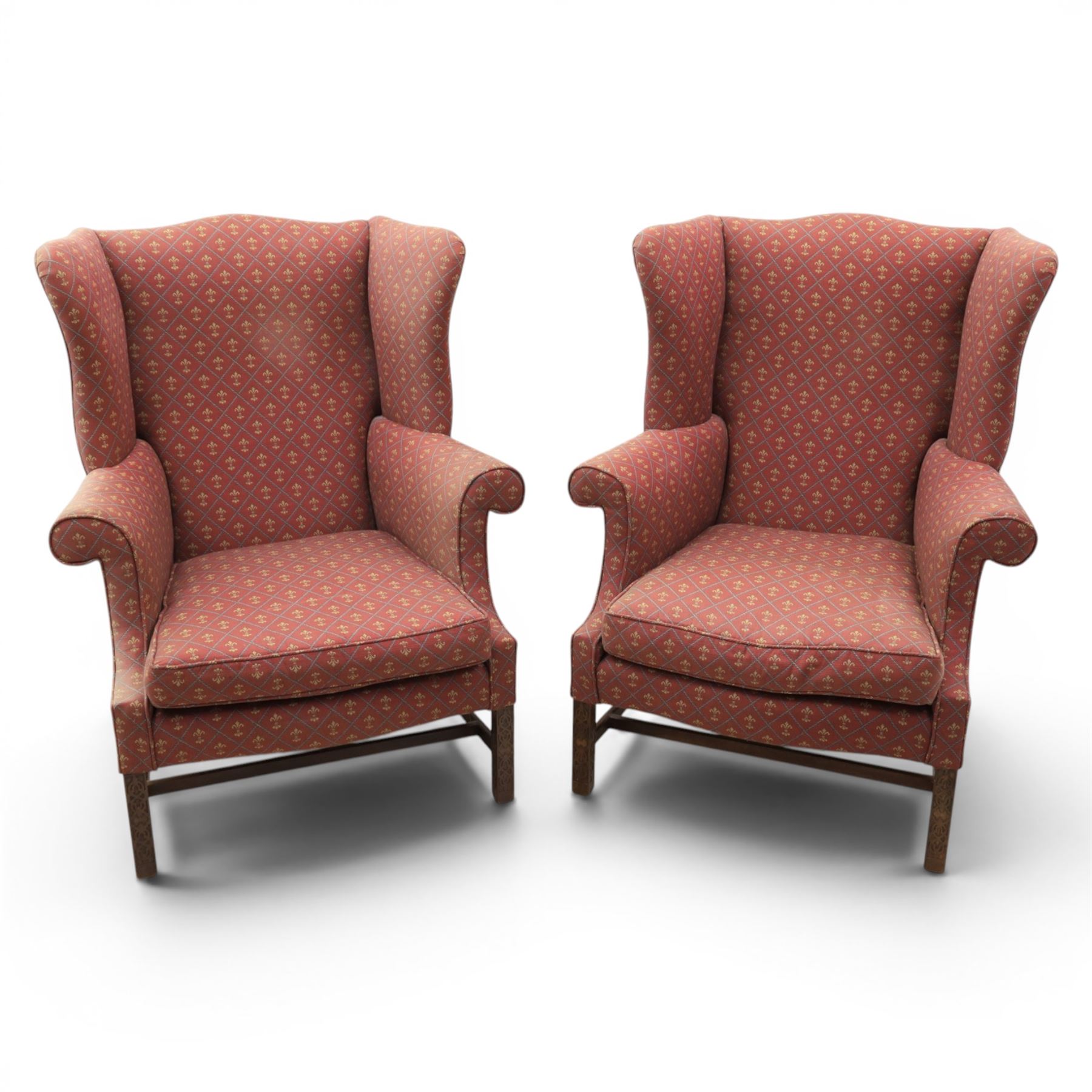 Georgian design wingback armchairs, the high backs flanked by shaped wings over padded scroll arms, upholstered in burgundy and gilt fleur-de-lys patterned fabric, loose cushion seats, raised on square tapering front supports