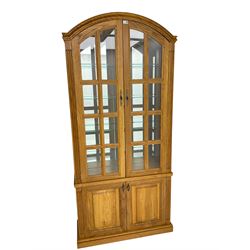 Light oak arched top display cabinet, mirrored interior enclosed by two glazed doors, double panelled cupboard below, on plinth base