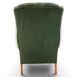 20th century green leather wingback button backed armchair, brass studded trim, with scrolled arms raised on oak supports